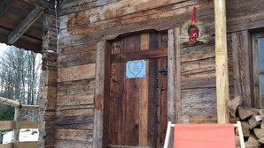 En rustik trästuga med en träveranda, en dörr med en hjärtformad skylt och en röd stol.
