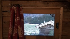 En stuga med träpanel på insidan, med ett fönster som vetter ut mot ett snötäckt landskap och en annan stuga.