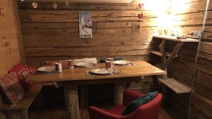 En inredning med träpanel, ett matbord för två personer, en bänk och en röd stol.