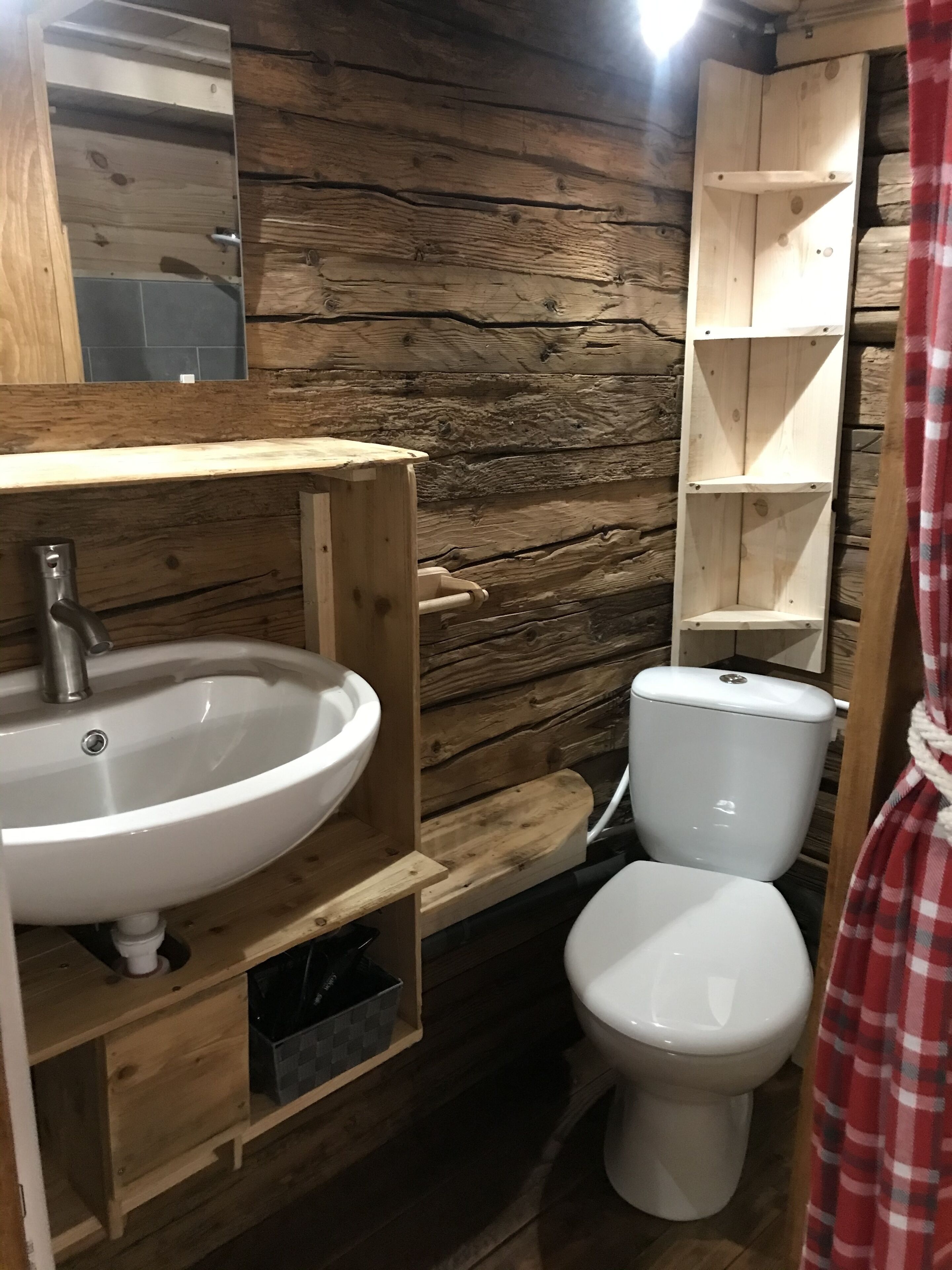 A wooden cabin-style bathroom with a white sink, toilet, and wooden shelves.