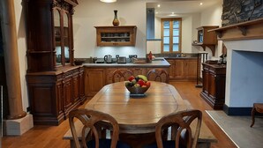 Een ruime keuken met houten kastjes, een grote eettafel en hangende hanglampen.