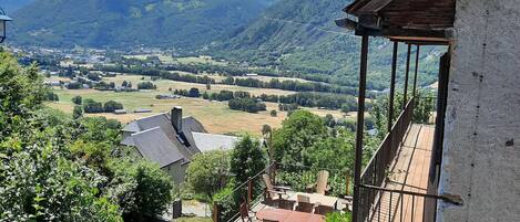 A wooden deck with outdoor furniture overlooking a valley and mountains.
