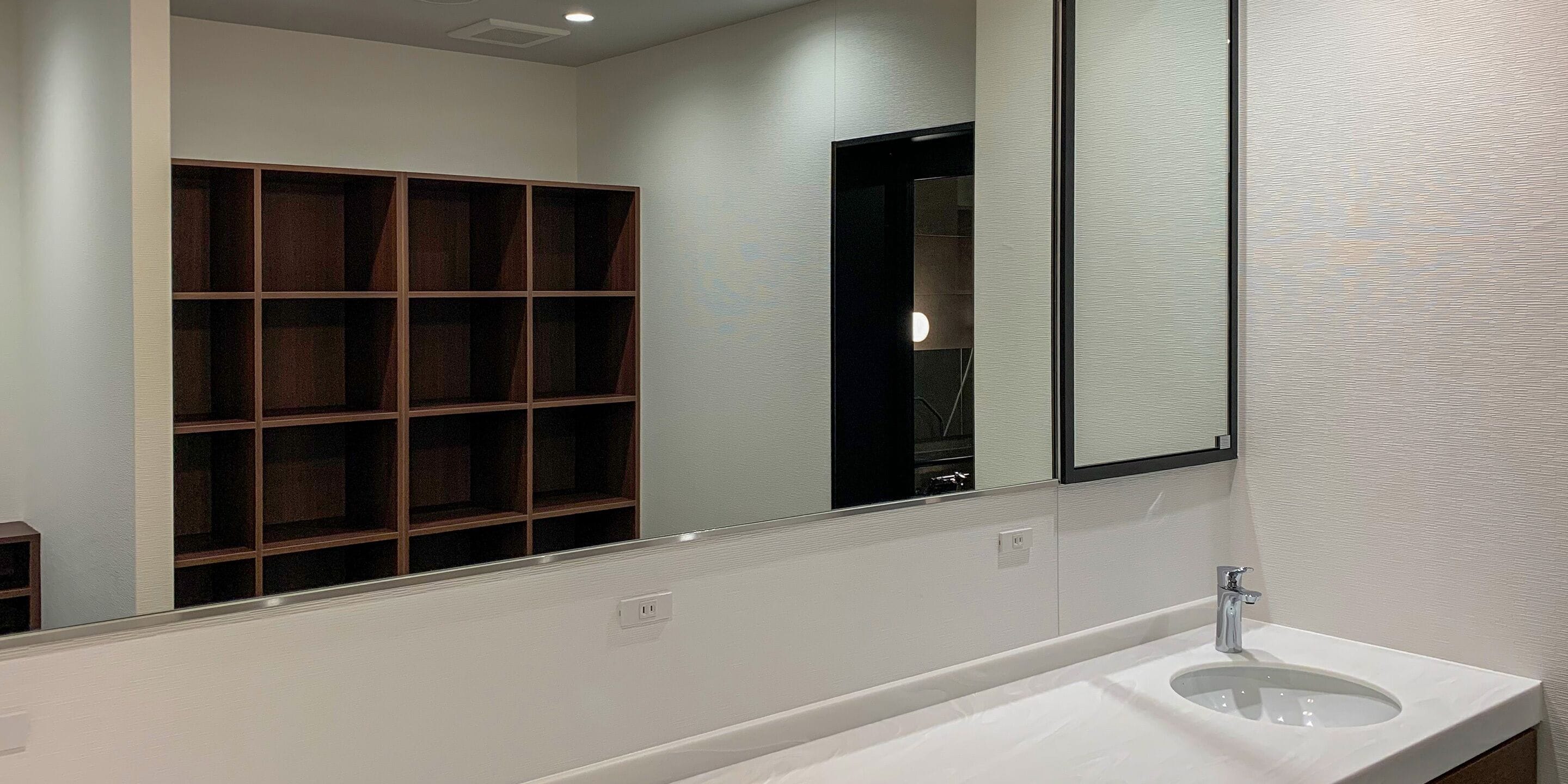 Une salle de bain avec un grand miroir, un lavabo blanc et une étagère en bois.