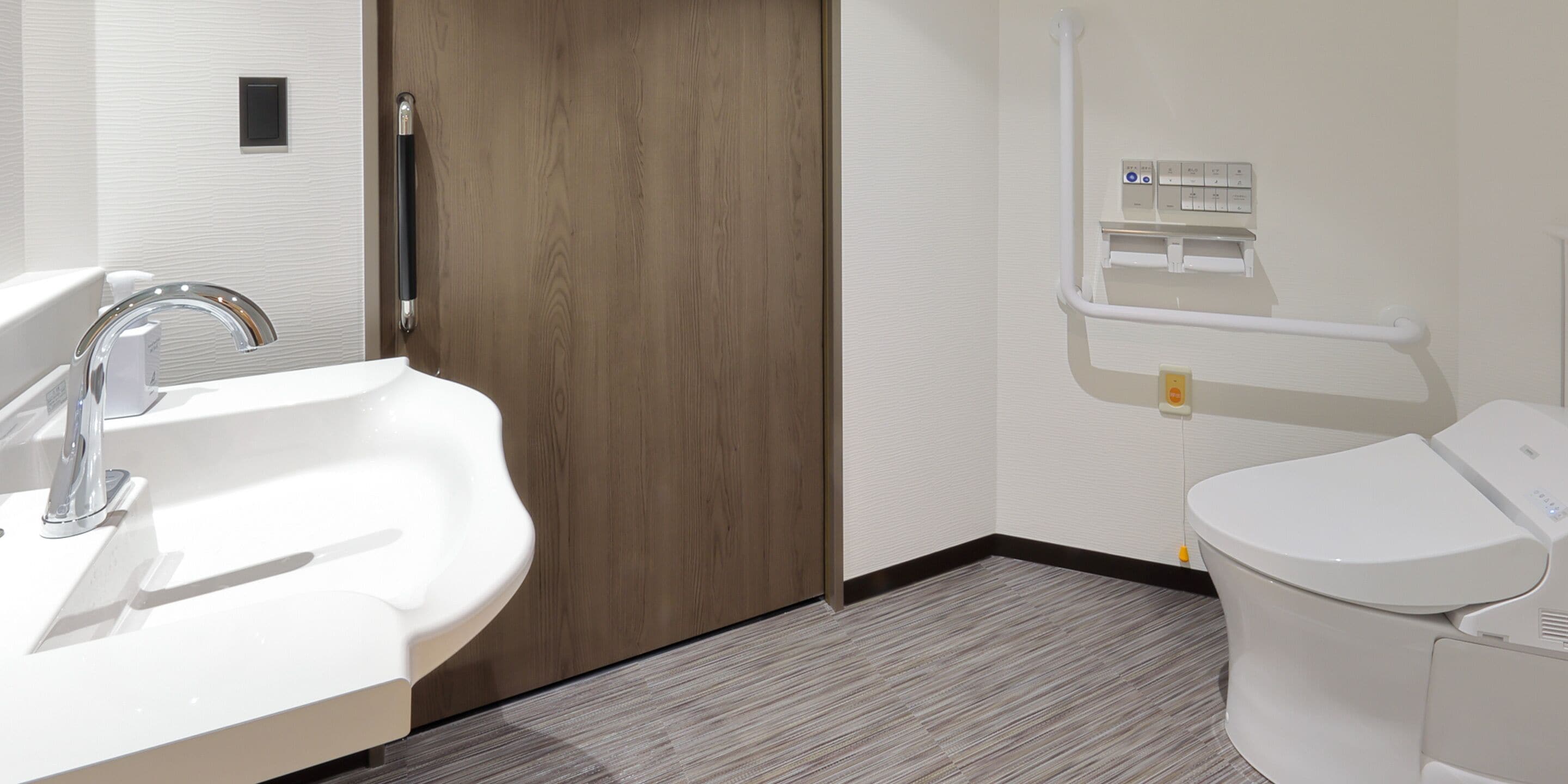 A modern bathroom with a sink, toilet, and a wooden door.