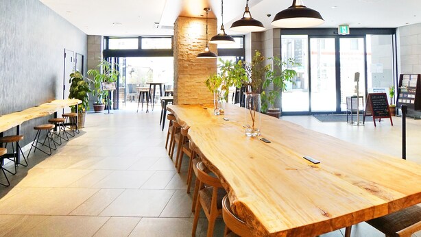 A spacious indoor area with a long wooden table and multiple chairs, surrounded by potted plants and pendant lighting. - HOTEL SUI KOBE SANNOMIYA by ABEST (Kobe)