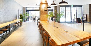 Un espace intérieur spacieux, doté d’une longue table en bois et de nombreuses chaises, agrémenté de plantes en pot et éclairé par des luminaires suspendus.