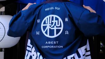 A person holding a blue jacket with "HOTEL SUI" and "ABEST CORPORATION" text.