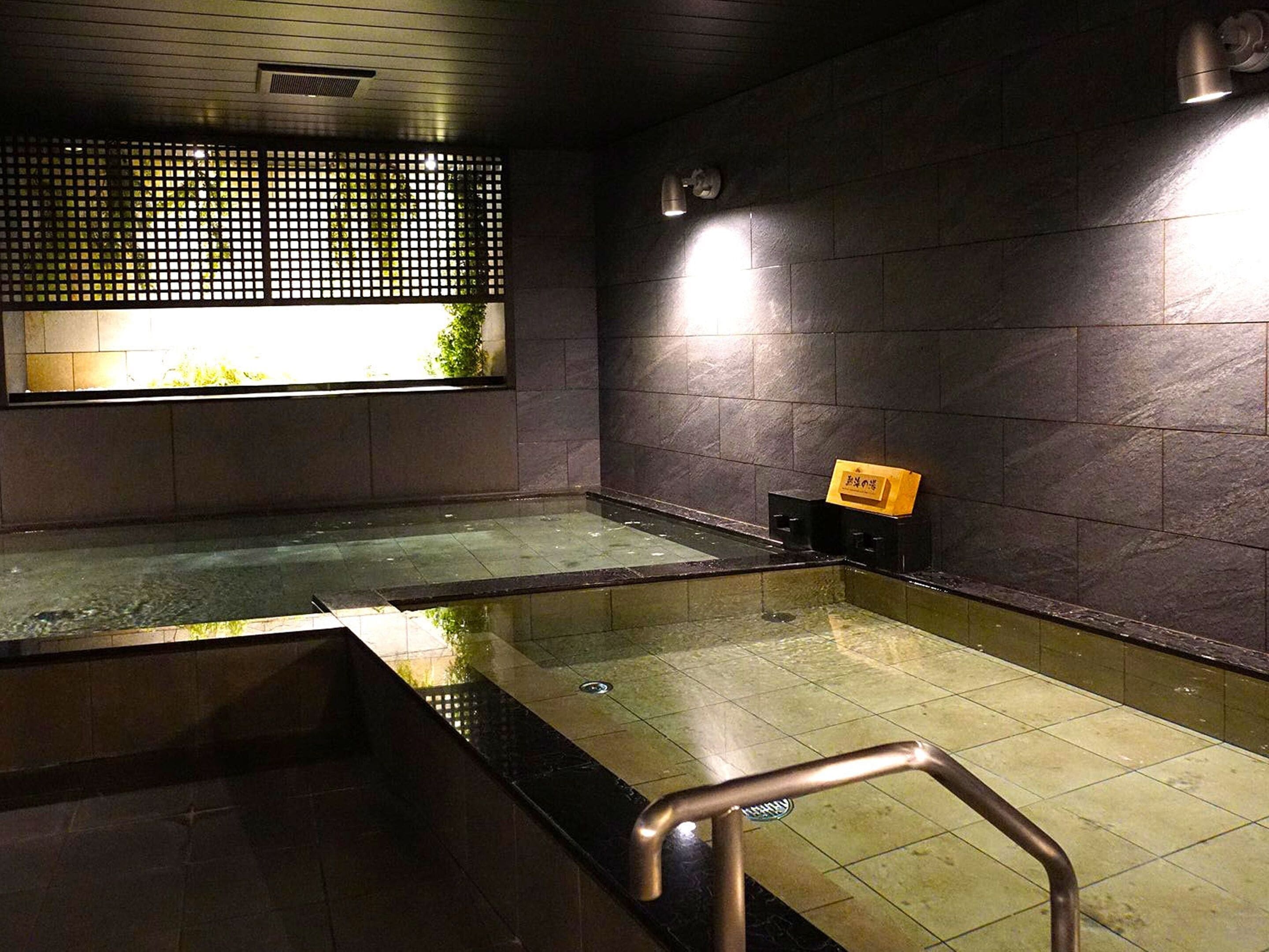 Ein moderner Poolbereich im Innenbereich mit Glasboden, dunklen Steinwänden und einer Holzwand mit Fenster.