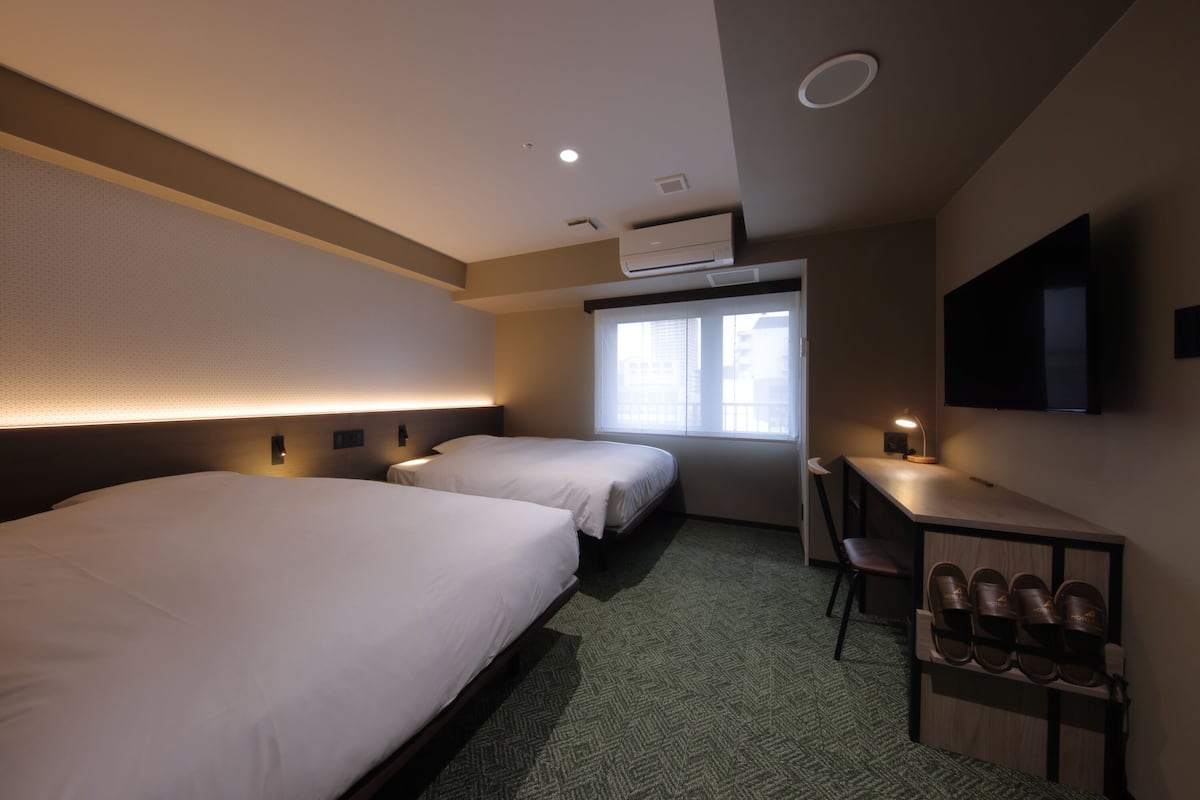 A hotel room with two beds, a desk, a chair, a TV, and a shoe rack.