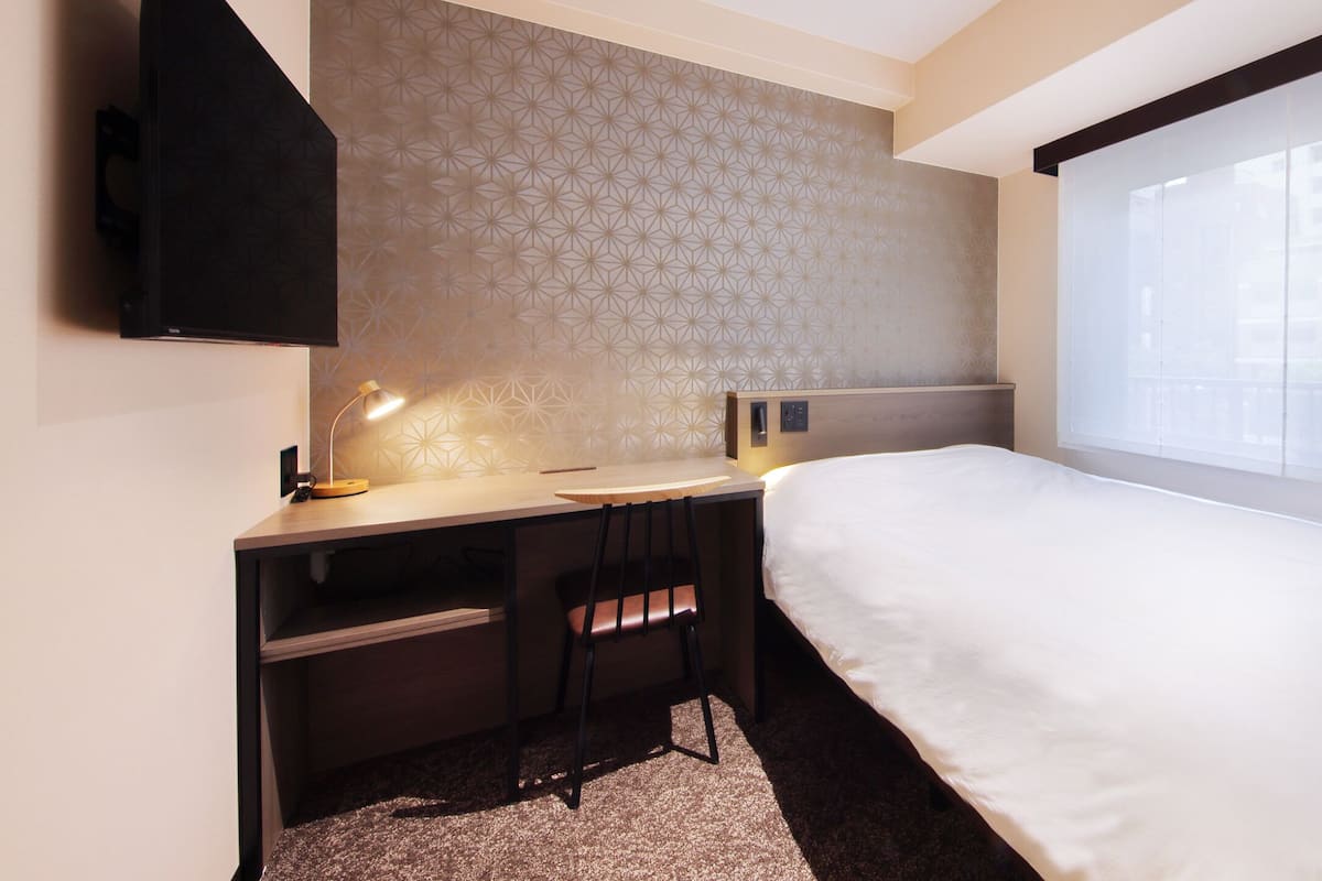 A hotel room with a bed, desk, chair, and a large window.