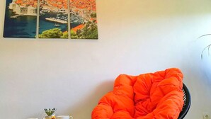 A room with a black chair, a small table with a white cup and saucer, and a framed picture of a coastal town. - Apartment Kola  (Dubrovacko Primorje)
