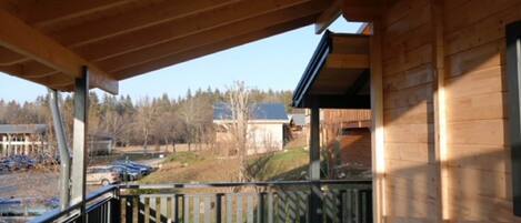 A wooden deck with a black railing, overlooking a parking area and buildings in the background.