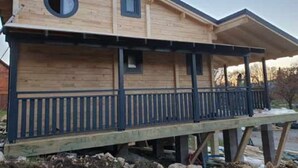 Une cabane en bois dotée d’une terrasse couverte et d’une fenêtre circulaire.