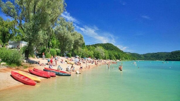 Une plage où des kayaks sont alignés sur le sable, des gens se détendent et on a une vue dégagée sur l’eau.