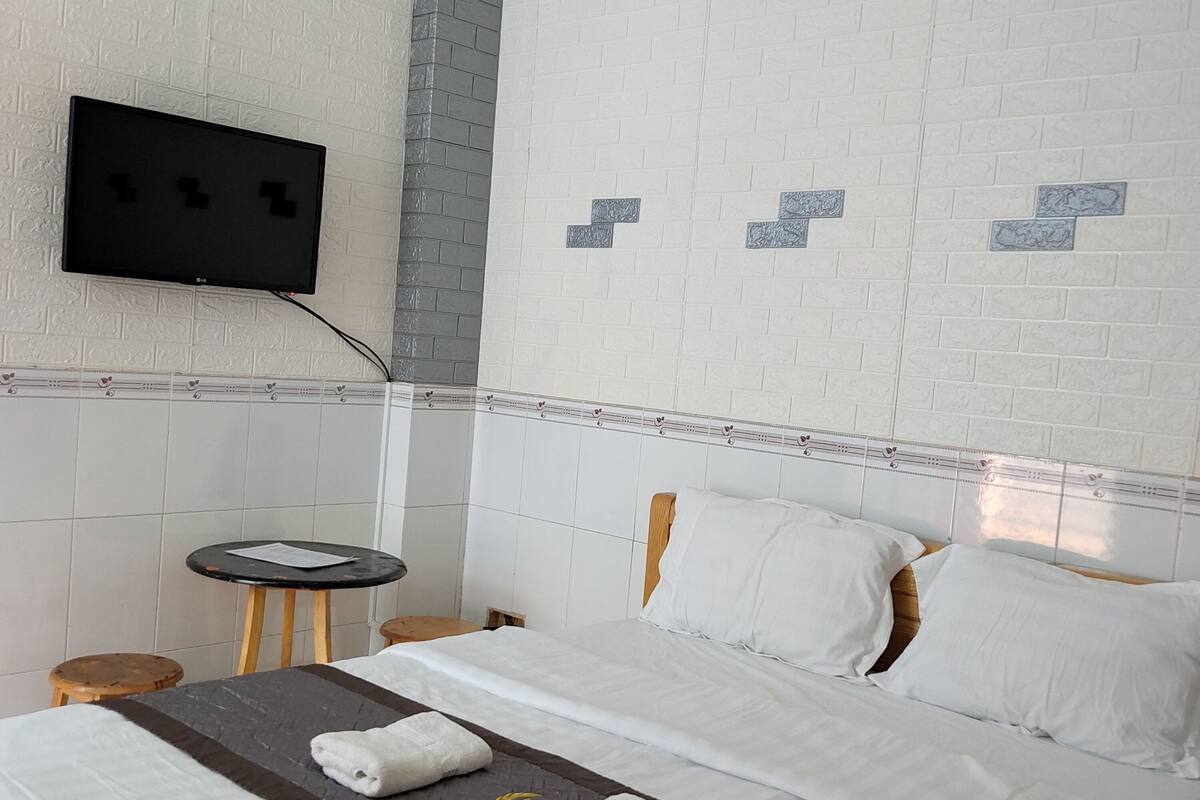 A hotel room with a bed, a TV mounted on the wall, a small round table, and a nightstand.