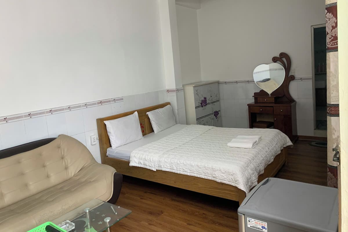 A bedroom with a bed, a wooden headboard, a bedside table, a mirror, a dresser, and a small table with a green object on it.