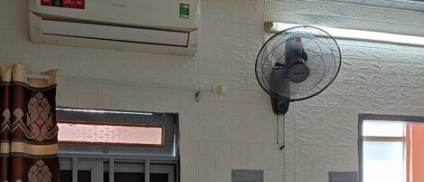 A room with a window, air conditioning unit, and a standing fan.