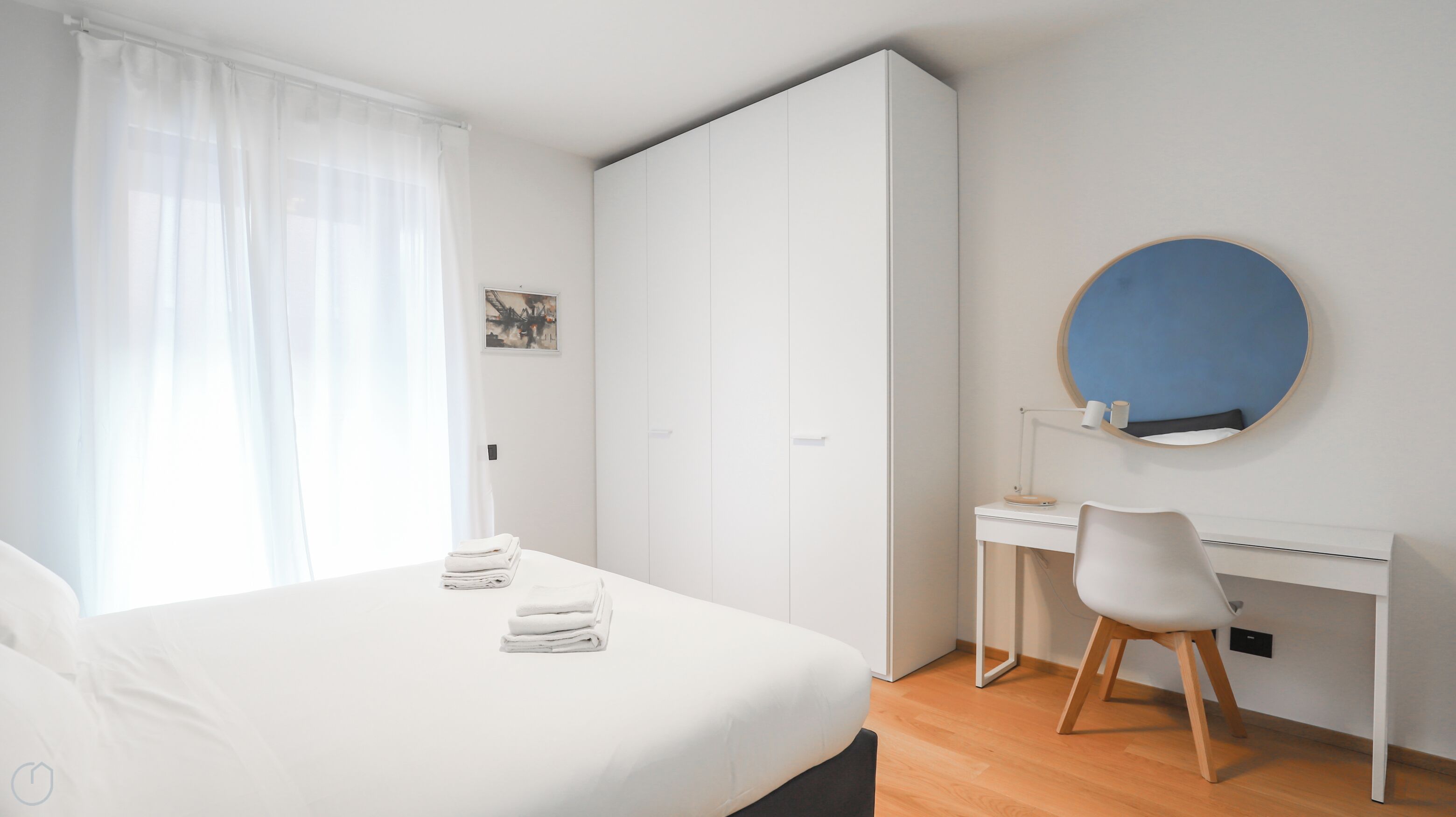 Ein Schlafzimmer mit Bett, Schreibtisch, Stuhl, Kleiderschrank und einem runden Spiegel an der Wand.
