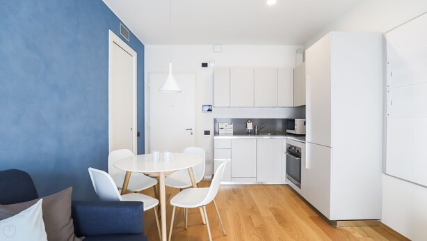 A compact kitchen with white cabinets, a microwave, and an oven. There is a dining area with a round table and four chairs. - Italianway - Lazzaro Papi 14 B (Milan)