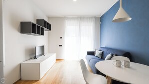 A modern living room with a TV, white furniture, a blue accent wall, and a dining area with two mugs. - Italianway - Lazzaro Papi 14 B (Milan)