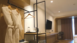 A hotel room with a wooden floor, a bed, a desk with a flat-screen TV, a mini-fridge, a microwave, and a hanging robe rack. - Sann Boutique Hotel (Chiang Rai)