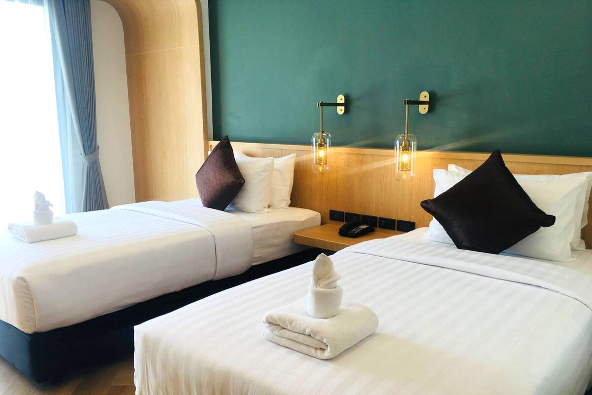 Habitación de hotel con dos camas, cabecera de madera, mesita de noche con teléfono y lámparas de pared.