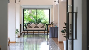 A modern interior with a sofa facing a large window, a tiled floor, and a small table with a vase. - Sann Boutique Hotel (Chiang Rai)