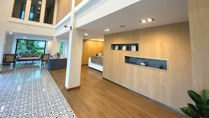 A spacious hotel lobby with a high ceiling, a reception desk, seating area, and a large window offering a view of greenery. - Sann Boutique Hotel (Chiang Rai)