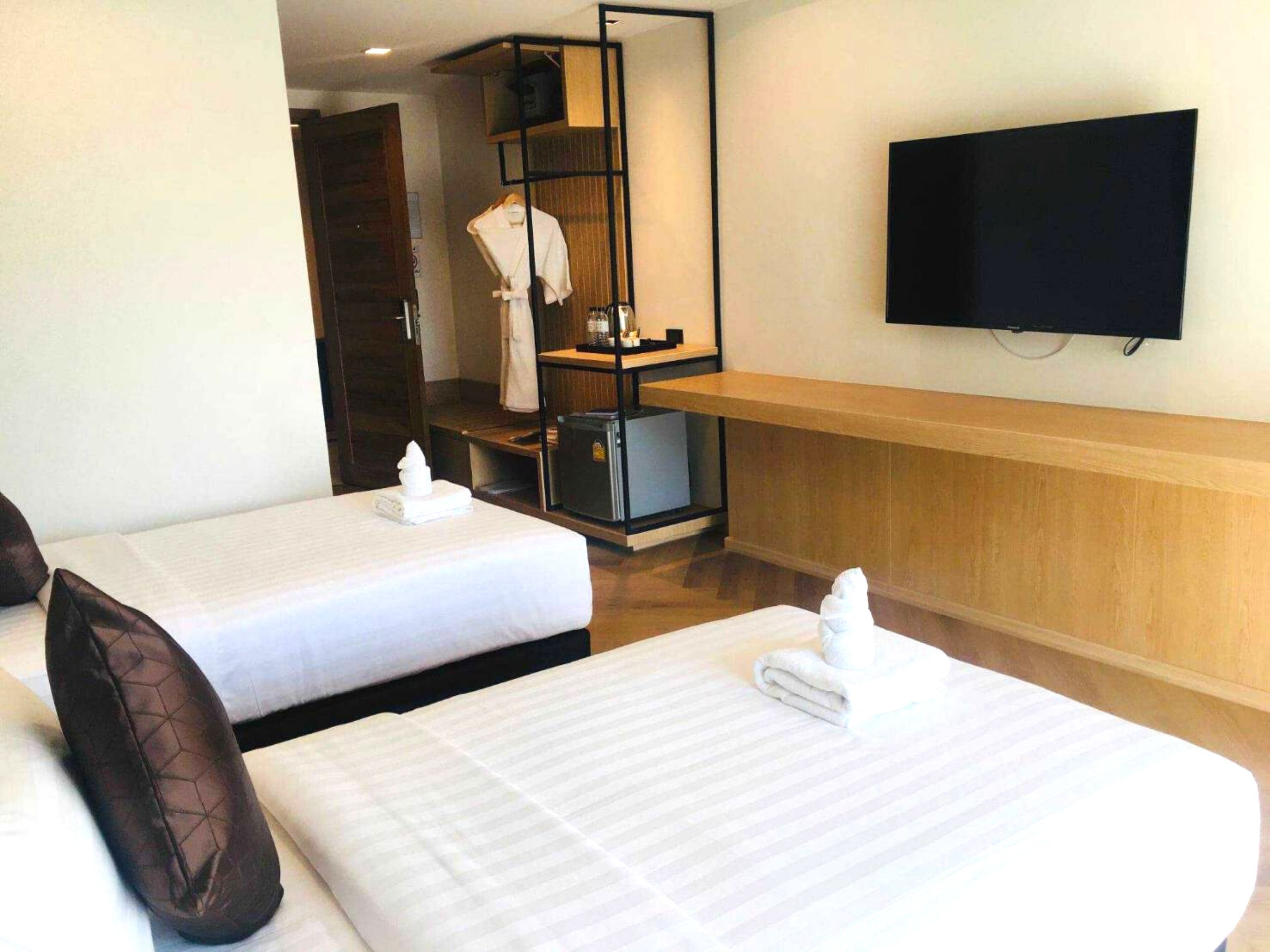 A hotel room with two beds, a TV, a minibar, and a bathroom visible through an open door.