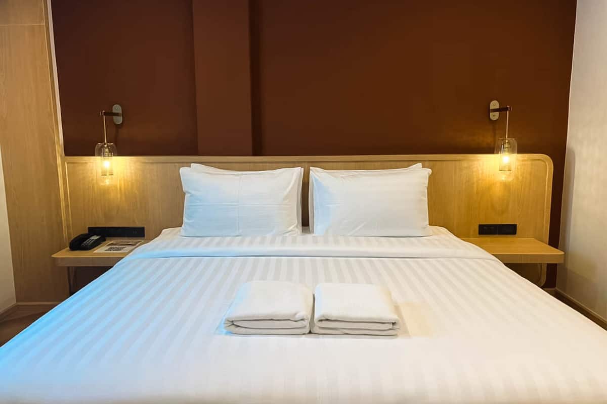 Una cama bien hecha con sábanas blancas y dos almohadas, flanqueada por mesitas de noche con lámparas.