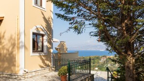 A stone-paved pathway leading to a building with a green metal railing and a potted plant. - Villa Federica by Rodostamo Collection (Corfu)