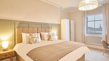 Een keurig opgemaakt slaapkamer met een groot bed, een bedlampje en een uitzicht op een stadsgezicht door een raam.