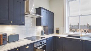Una cucina moderna con mobili scuri, un piano di lavoro bianco, un forno integrato e una finestra con vista sugli edifici.