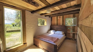 A rustic wooden bedroom with a bed, two windows, and a small shelf.