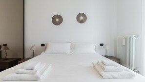 Ein Hotelzimmer mit einem großen Bett, zwei Wandleuchten, einem Heizkörper und ordentlich gefalteten Handtüchern auf dem Bett.