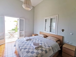 Ein Schlafzimmer mit Bett, Nachttischen, einem Fenster mit Rollläden und einer Tür zum Balkon.