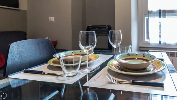 Een eettafel gedekt met kleurrijke borden, wijnglazen en bestek.