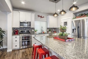 Una cocina moderna con armarios blancos, electrodomésticos de acero inoxidable, encimera de granito y taburetes rojos.