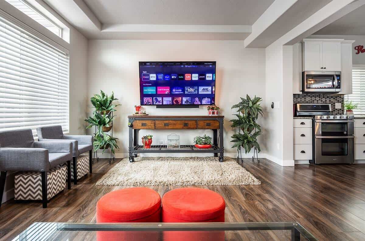Una sala de estar moderna con un televisor de pantalla plana, una mesa de centro, otomanas rojas y una cocina con electrodomésticos.
