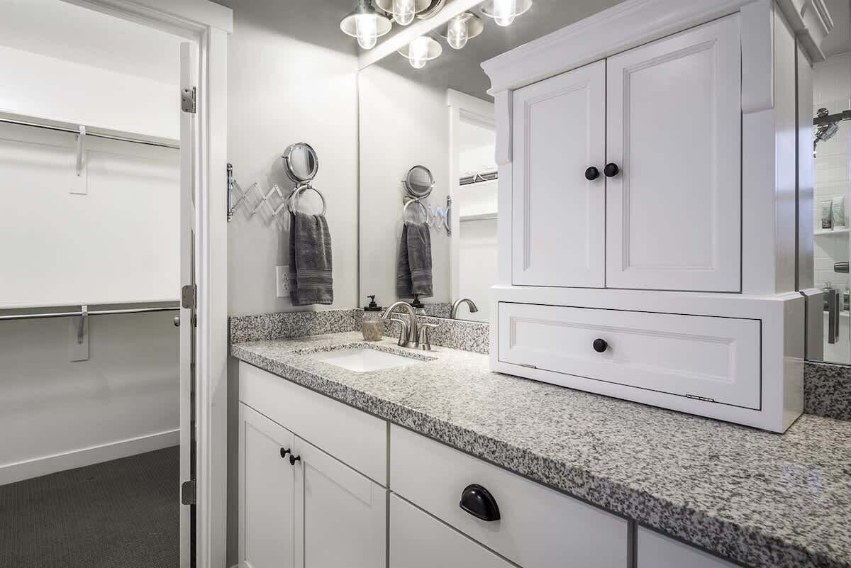 A bathroom with a granite countertop, a white sink, a mirror, and a cabinet with a microwave.