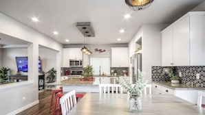 Uma cozinha moderna com armários brancos, uma ilha central e uma área de refeições com cadeiras vermelhas.