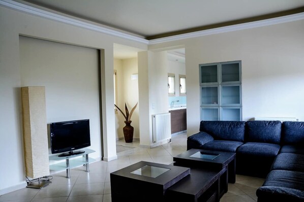 A modern living room with a flat-screen TV, a dark blue sofa, and a glass coffee table.