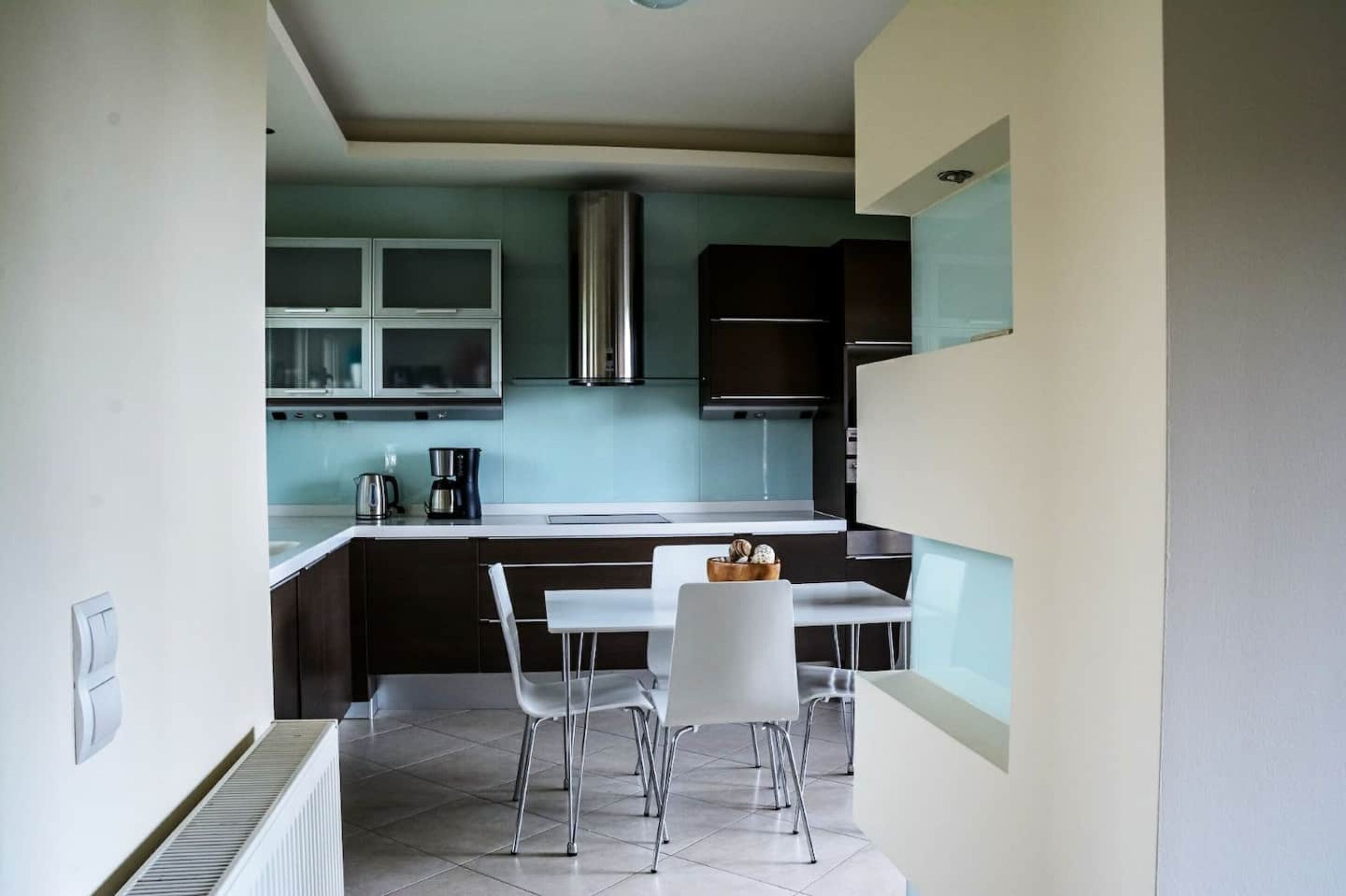 Una cocina moderna con comedor, que cuenta con una campana de acero inoxidable, una cafetera y una pequeña mesa con sillas.