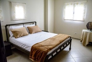 A single bed with a wooden frame, white bedding, and a brown throw blanket.