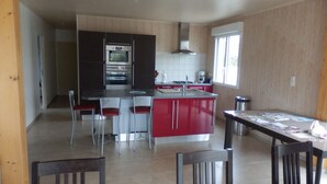 A modern kitchen with a central island, red and black cabinets, stainless steel appliances, and a dining area with two chairs. - FREHEL HOUSE (Fréhel)