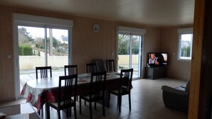 A dining area with a table and chairs, a television, and large windows. - FREHEL HOUSE (Fréhel)