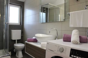 A modern bathroom with a toilet, sink, and washing machine. - Holiday Home Ela (Nerezise)