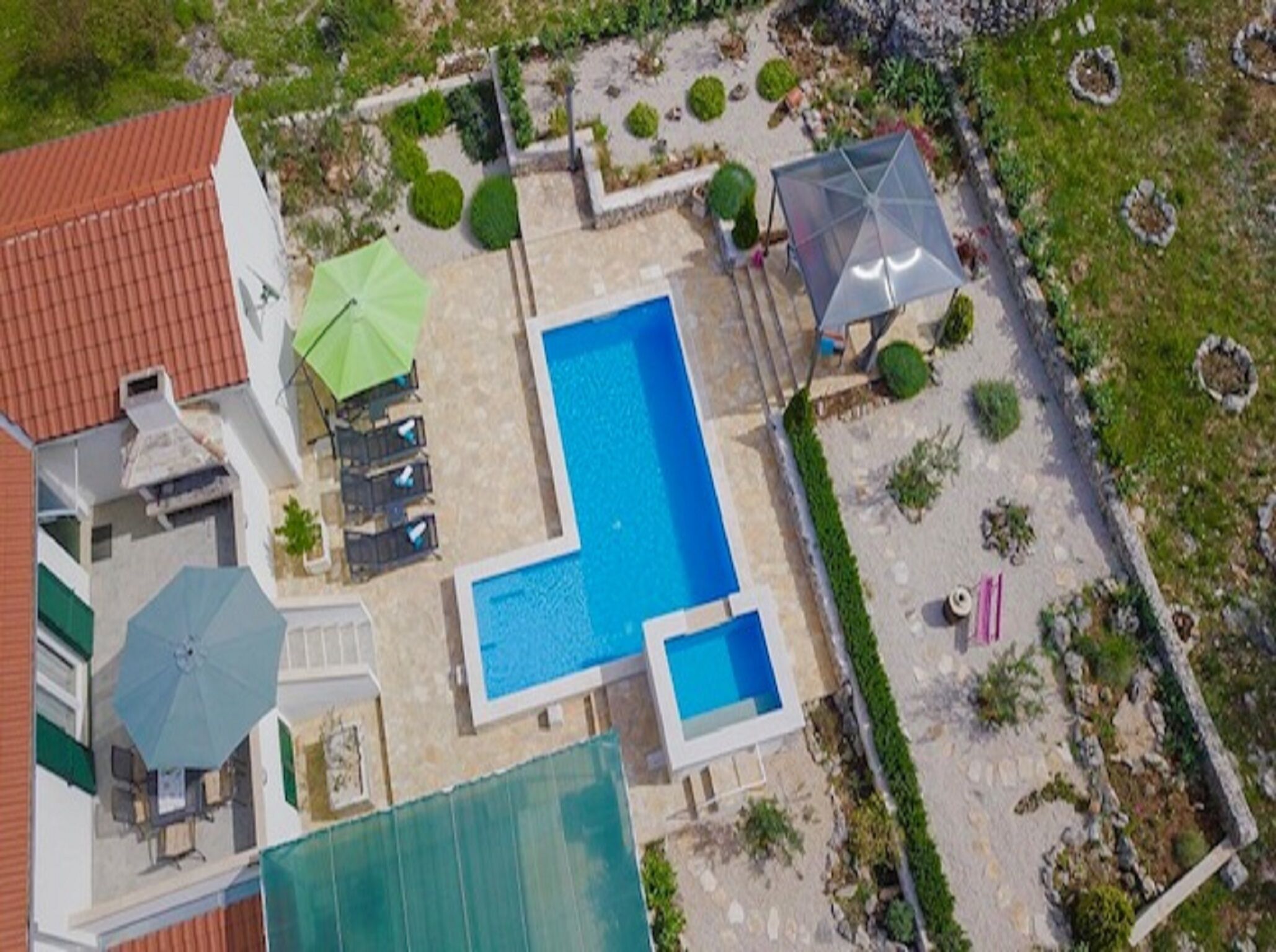 Ein großer rechteckiger Pool, umgeben von einer Terrasse mit Liegestühlen und Sonnenschirmen.