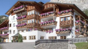 Un immeuble à plusieurs étages, doté de balcons en bois, d’une fondation en pierre et surplombant un paysage montagneux.