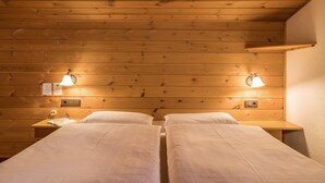 Une chambre dans un chalet en bois, avec deux lits, des lampes de chevet et une petite table sur laquelle se trouve un livre.
